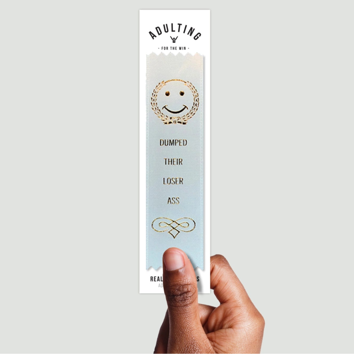 A hand holding a white satin award ribbon with gold foil stamping that reads