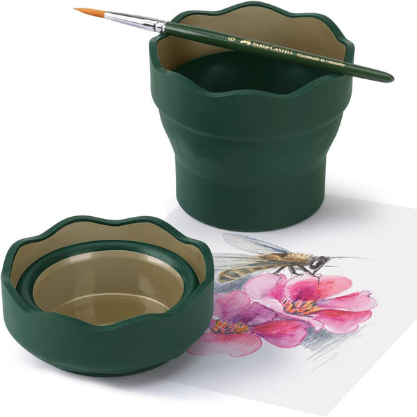 A collapsible green water cup with a paintbrush resting on top, displayed next to a piece of paper with a floral artwork on it.