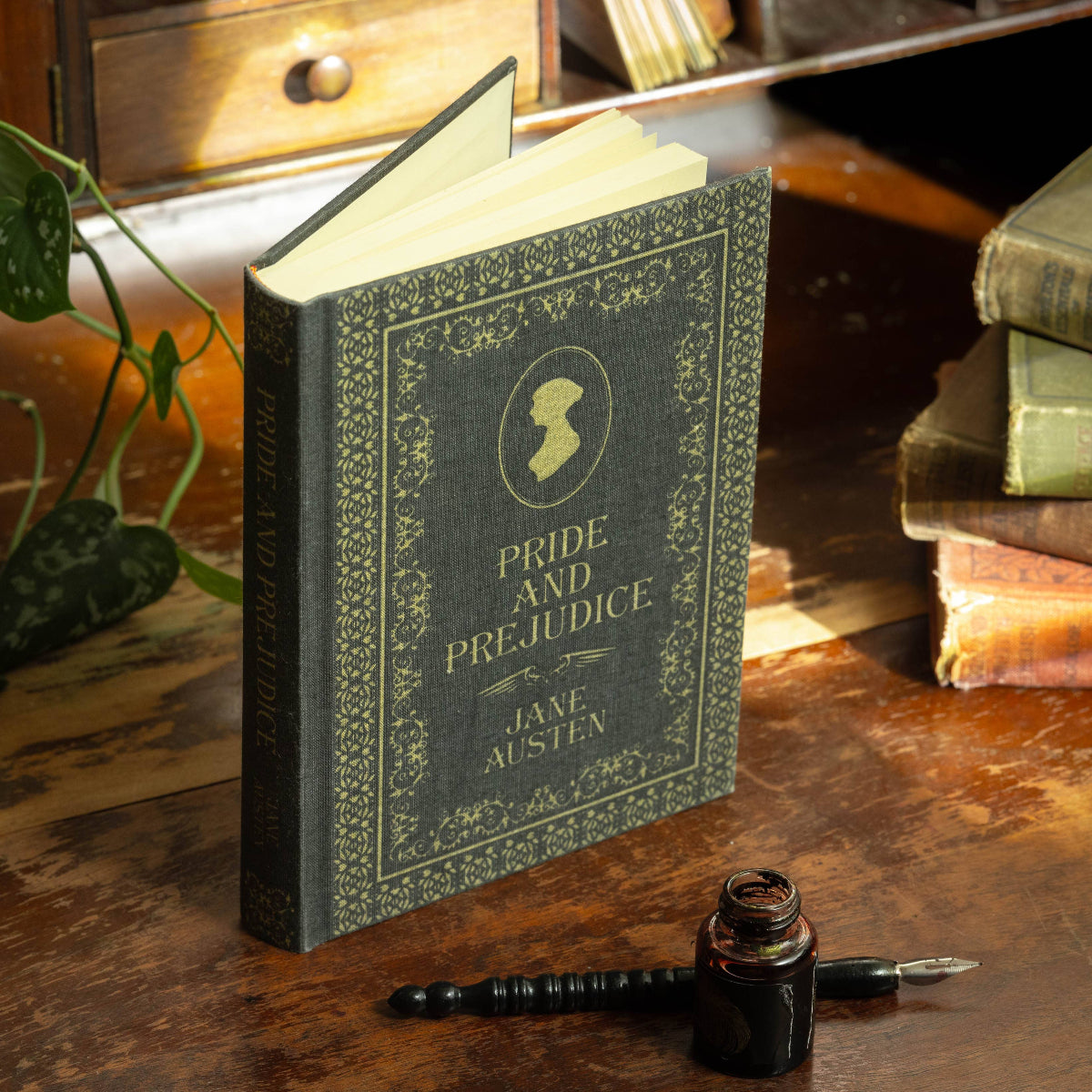 A journal designed to resemble 'Pride & Prejudice' by Jane Austen, with an embossed cover and a pen beside it, placed on a wooden surface with books in the background.