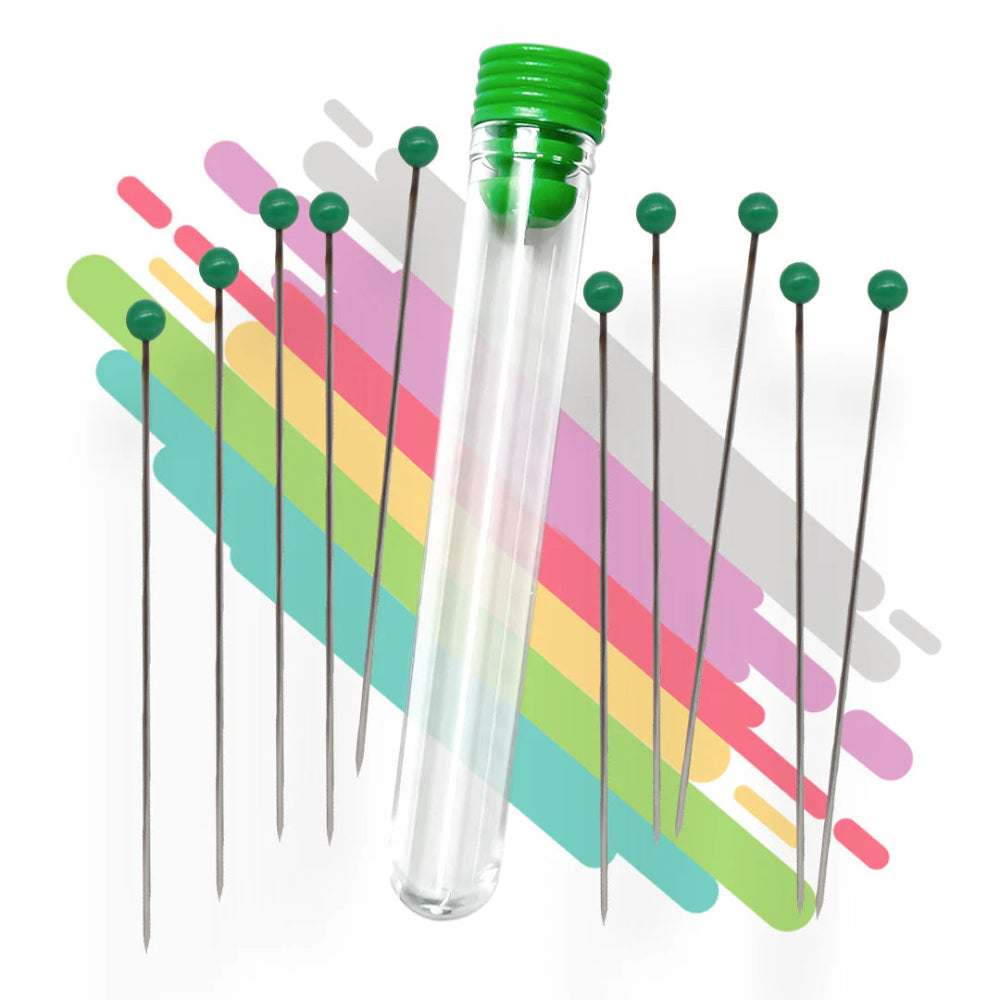 A set of stainless steel cleaning pins with green caps, displayed in front of a colorful background, and packaged in a clear plastic tube.
