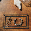 Jewelry on a glass display stand with a rock and glass container on a wooden surface