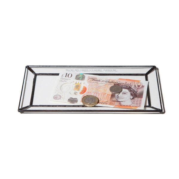 Glass money tray with British pound notes and coins on a white background
