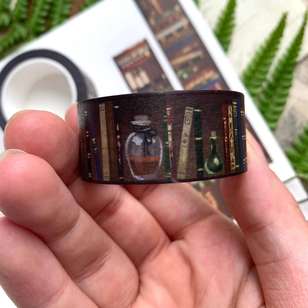 Hand holding a roll of washi tape with a design of books and potion bottles.
