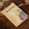 Book titled 'The Little Prince' on a wooden surface with a key.