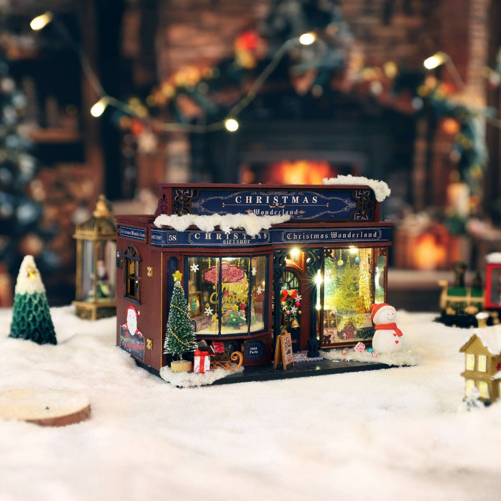 Decorative Christmas shop model with lights and snow effect in a festive setting.