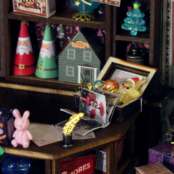 Miniature Christmas decorations on a shelf with a focus on a box containing a yellow rabbit figure.