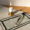 Glass tray with a candle and a small bottle on a textured surface.