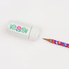 A white pencil sharpener with a green and pink floral design, shown next to a colorful patterned pencil on a clean white background.