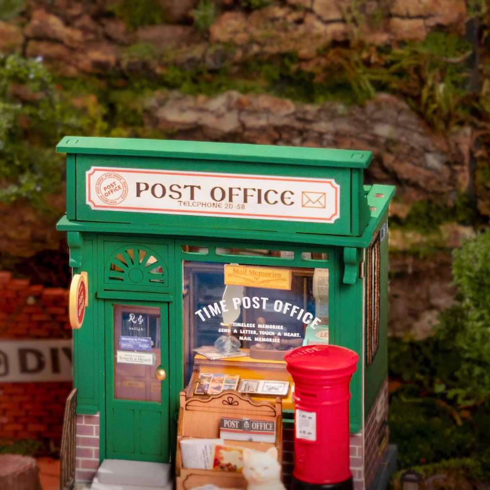 Model of a post office with a red mailbox against a natural background