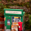 Model of a post office with a red mailbox against a natural background