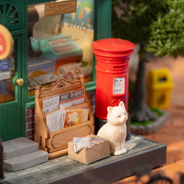 Miniature post office scene with a red mailbox, newspaper stand, and small cat figurine.