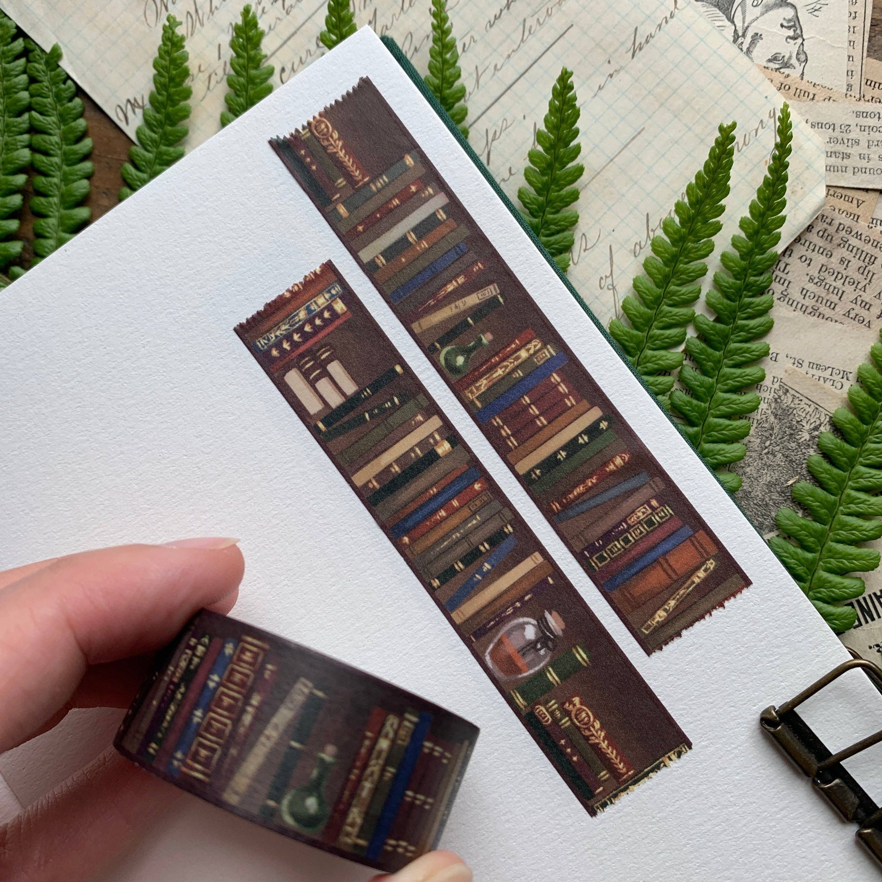 Decorative book-themed washi tape with a hand holding it, set against a textured background with greenery.