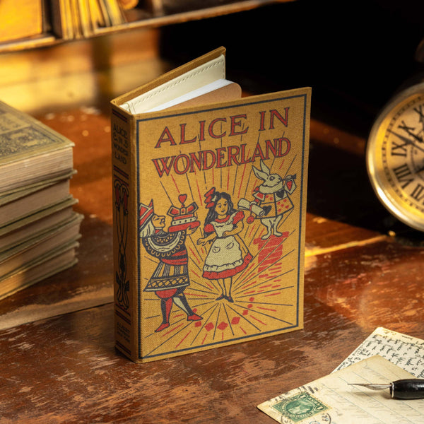 Miniature book titled 'Alice in Wonderland' on a wooden surface with vintage items.