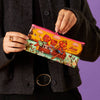 A person wearing a dark charcoal cardigan holds a colorful zippered pouch featuring cartoon teddy bears in a boat with the text 'Bear Adventure' against a solid purple background.