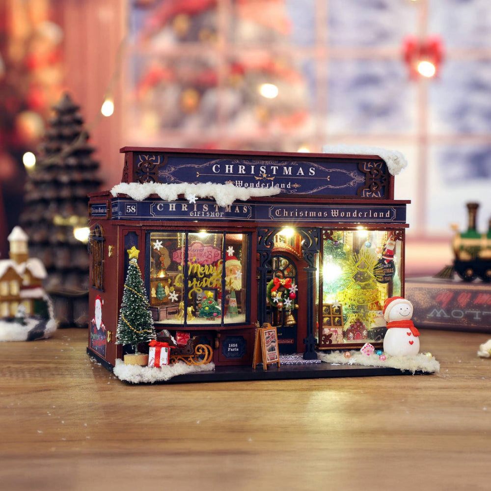 Miniature Christmas-themed store model with festive decorations on a wooden surface.