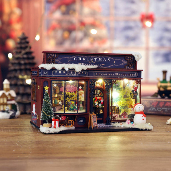 Miniature Christmas-themed store model with festive decorations on a wooden surface.