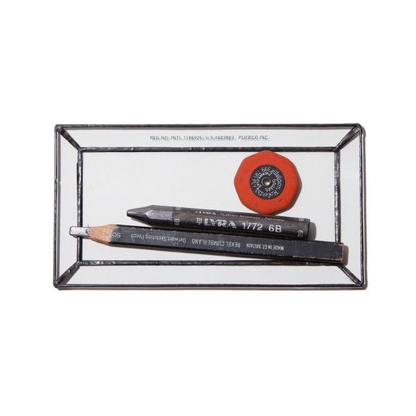 Three pencils and a red circular object in a glass display case on a white background